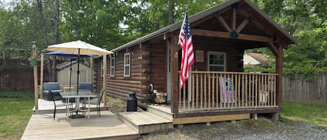 Una cabaña de madera con un porche, una bandera y un patio con mobiliario exterior.