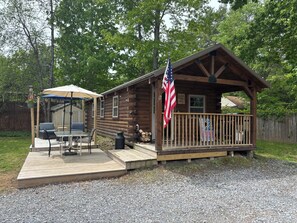 A wooden cabin with a porch, a flag, and a patio with outdoor furniture. - Cabin with big fenced yard-firepit-walking distance to Sacandaga lake- pets ok (Broadalbin)