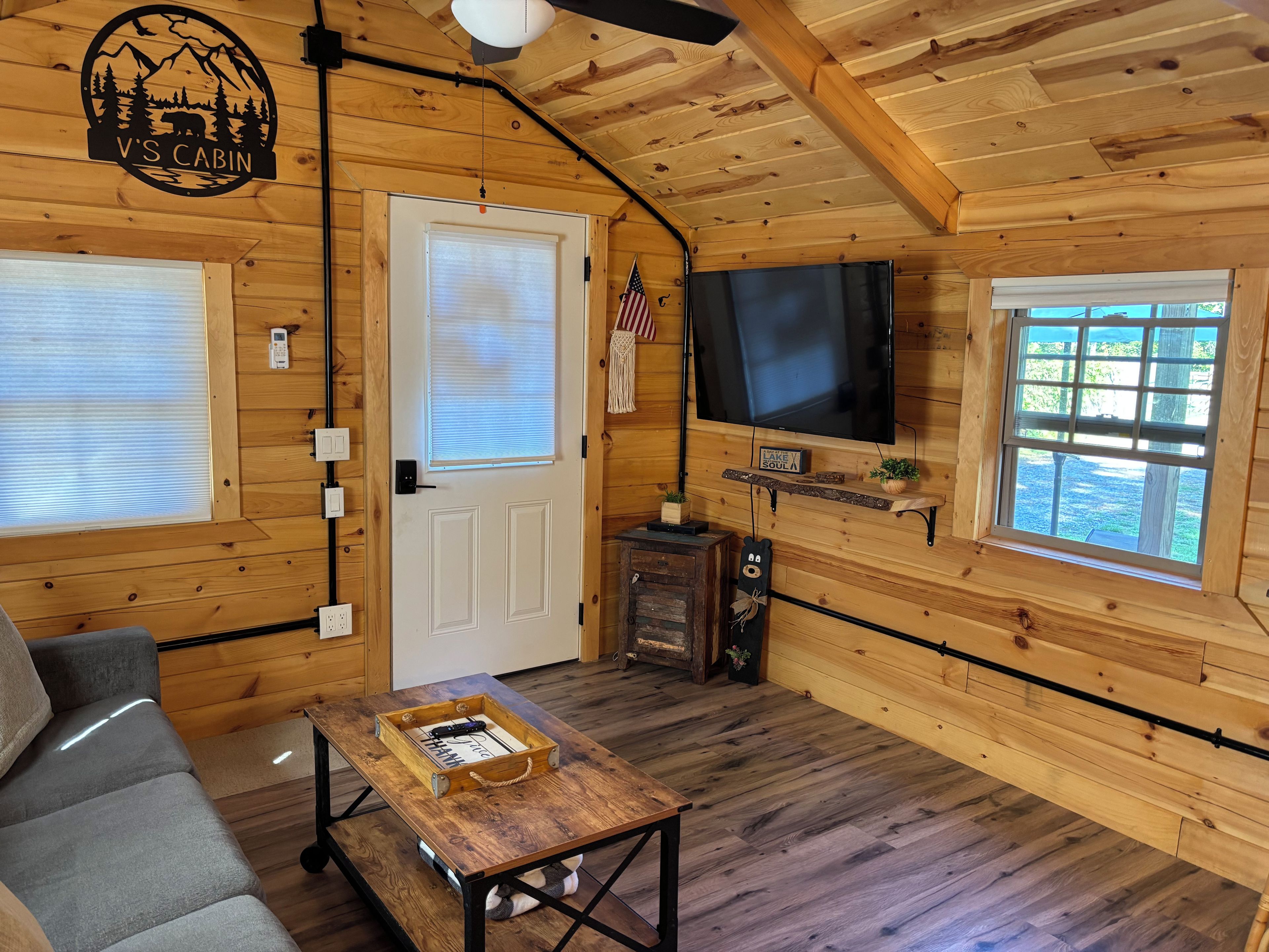 A cabin interior with a television, a wooden table, a sofa, and a door with a window.