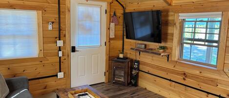 A cabin interior with a television, a wooden table, a sofa, and a door with a window.