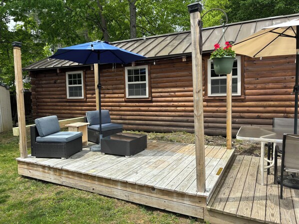 Une terrasse en bois avec des meubles d’extérieur, un parasol bleu et un pot de fleurs suspendu.