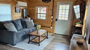 A cabin interior with a sofa, coffee table, wooden flooring, and a TV. - Cabin with big fenced yard-firepit-walking distance to Sacandaga lake- pets ok (Broadalbin)