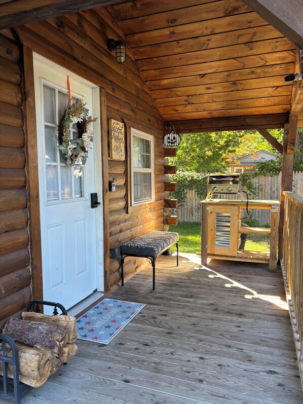 A wooden cabin with a porch, a bench, a barbecue grill, and a welcome mat.
