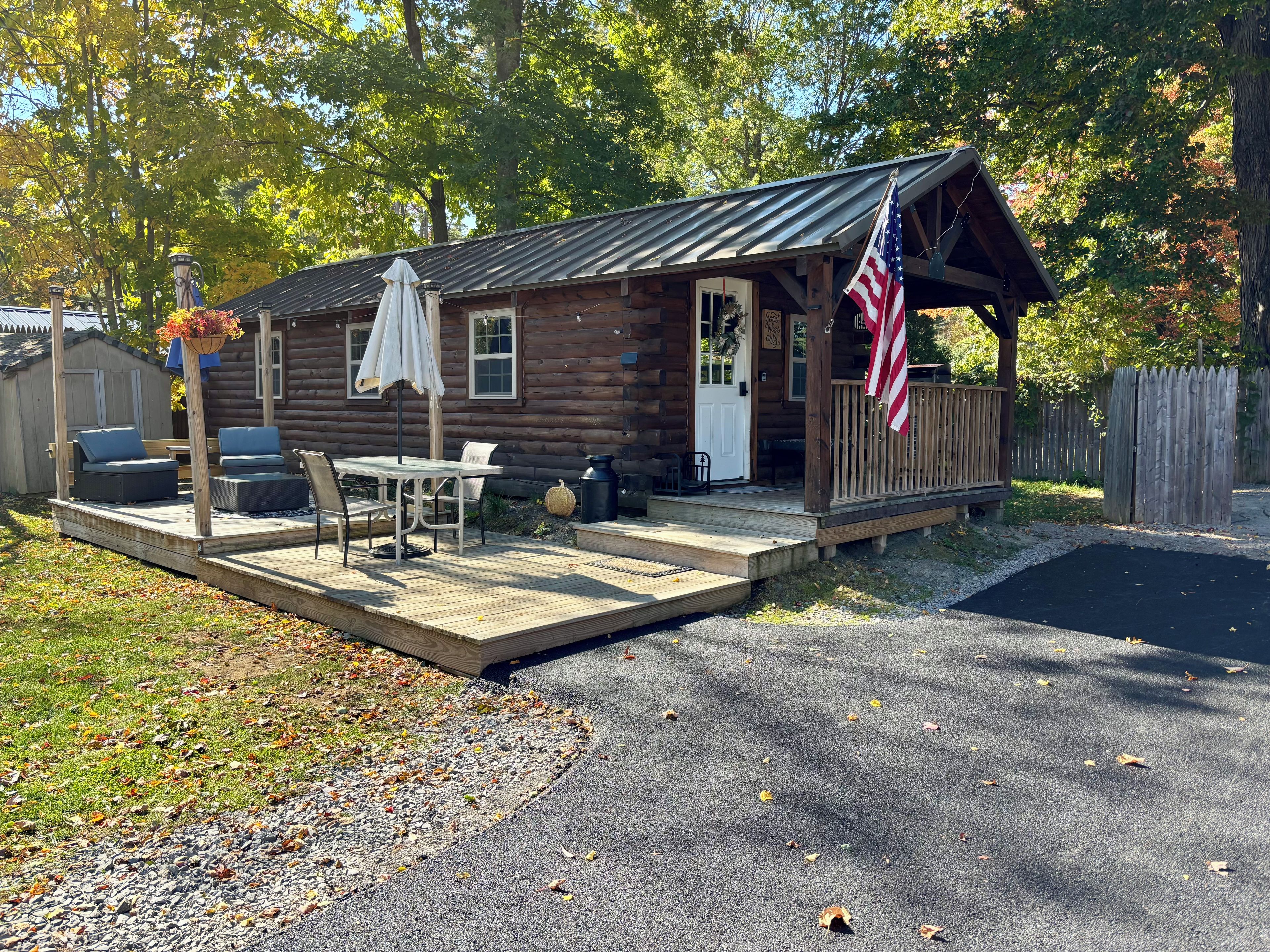 Een houten blokhut met een veranda, een tafel en stoelen, en een Amerikaanse vlag.