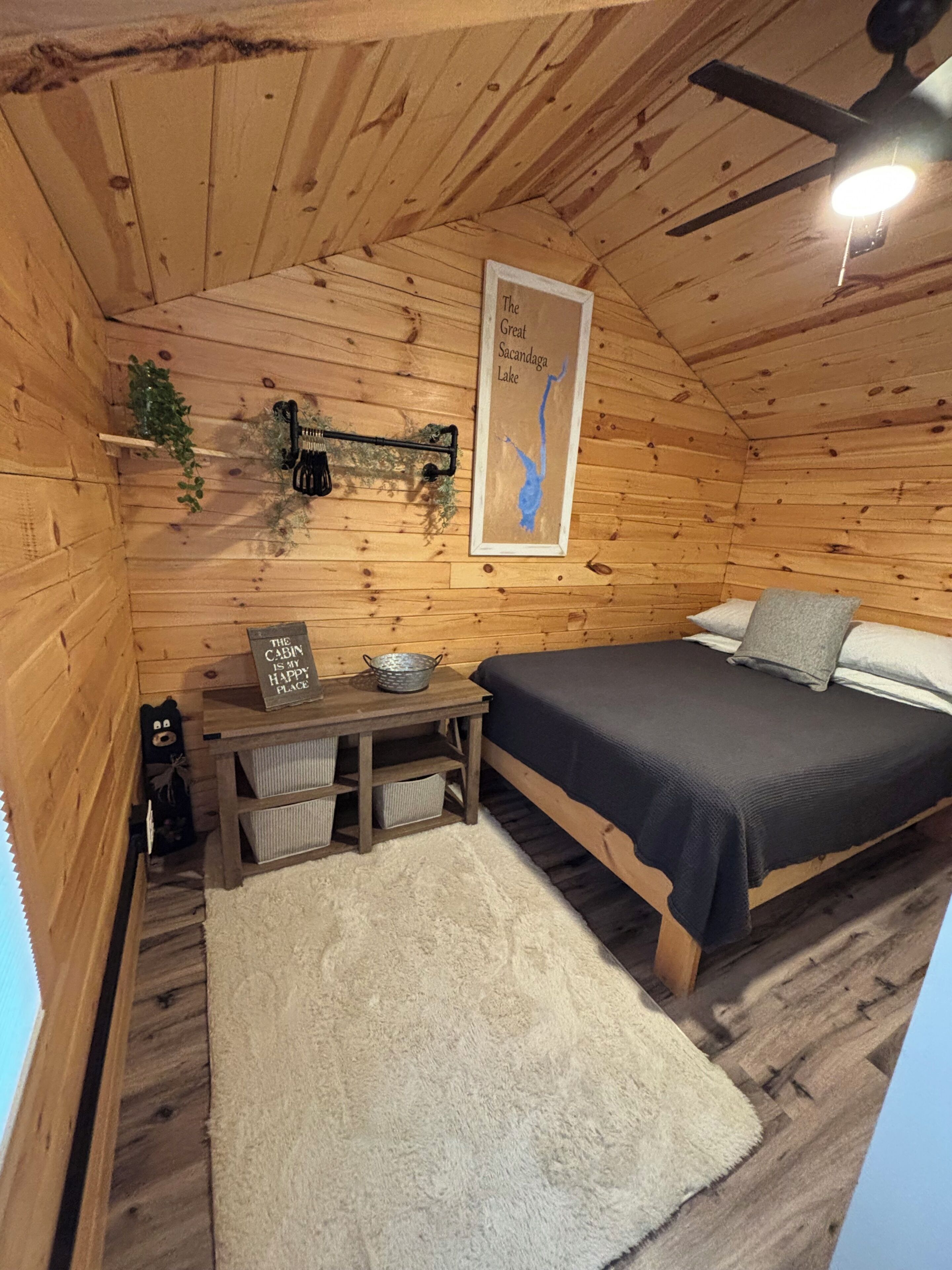 Een gezellig houten kamer met een bed, een klein tafeltje met een mand, een inlijsting kaart aan de muur en een plafondventilator.
