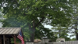 A gravel path leading to a wooden cabin with an American flag, surrounded by a wooden fence and trees. - Cabin with big fenced yard-firepit-walking distance to Sacandaga lake- pets ok (Broadalbin)