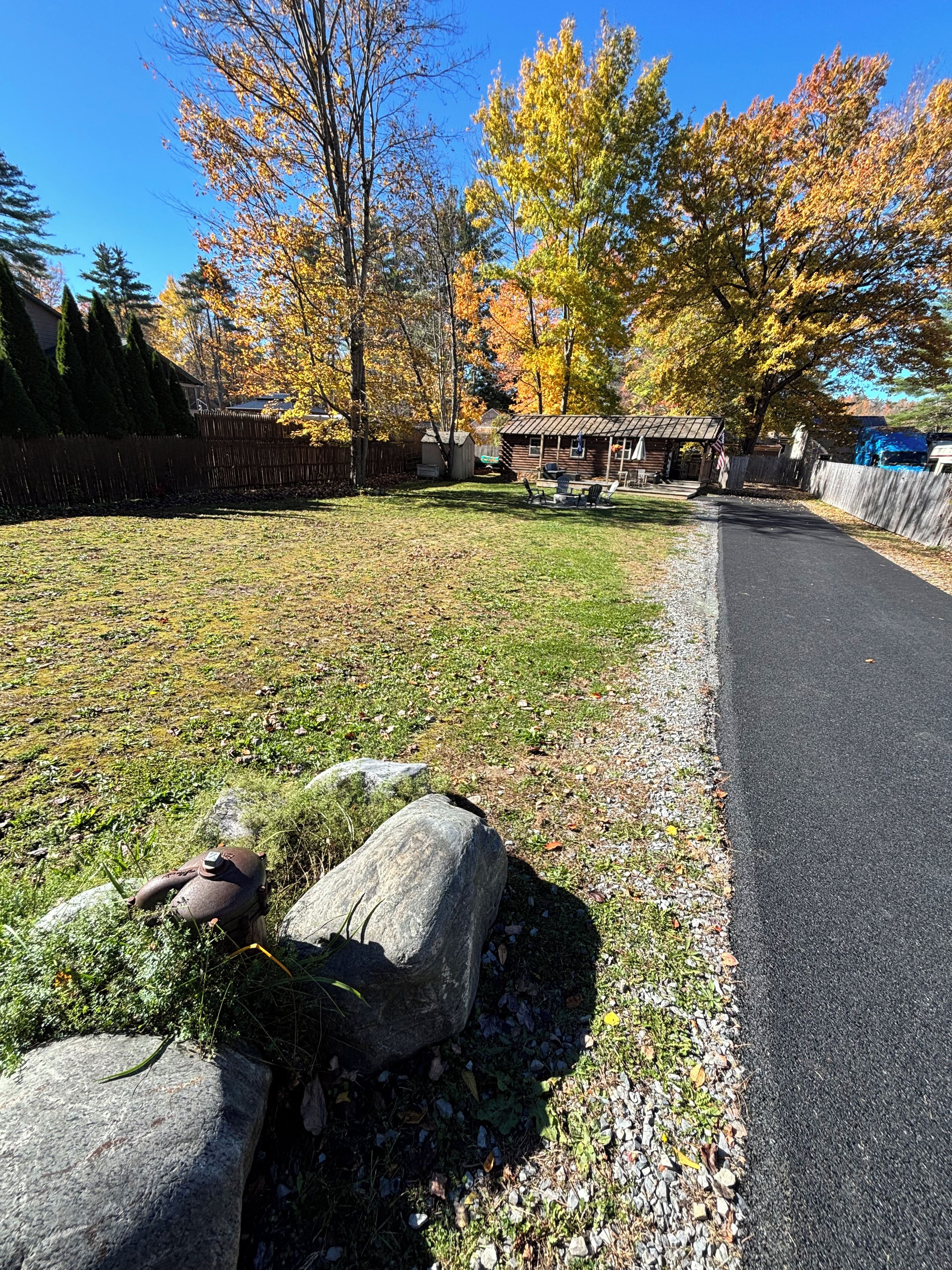 Un quartier résidentiel avec une allée pavée, une clôture en bois et une pelouse agrémentée d’arbres aux couleurs automnales.