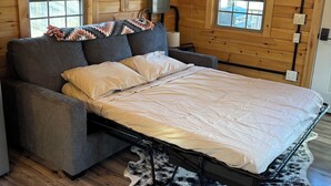 A cozy room with a bed, a sofa, and a ceiling fan. - Cabin with big fenced yard-firepit-walking distance to Sacandaga lake- pets ok (Broadalbin)