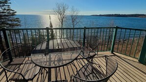 Una terraza con sillas de metal y una mesa con vista a un cuerpo de agua.
