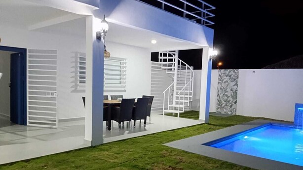 Une terrasse extérieure moderne avec une piscine, un coin repas comprenant des chaises et une table, ainsi qu’un banc en bois.