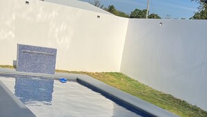 Une piscine avec une terrasse carrelée et un mur blanc en arrière-plan.