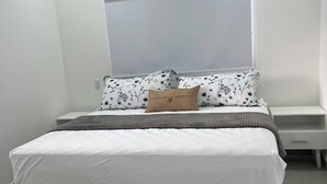 Une chambre moderne avec un grand lit, une fenêtre avec des stores, une table de chevet et un appareil de climatisation.