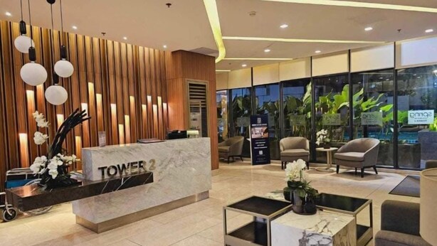 A modern hotel lobby with a reception desk labeled "TOWER 2", seating area, and large windows with indoor plants. - Cozy and Comfy Retreat with Balcony (Paranaque)