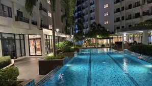 A swimming pool with tiled edges, surrounded by greenery and buildings. - Cozy and Comfy Retreat with Balcony (Paranaque)