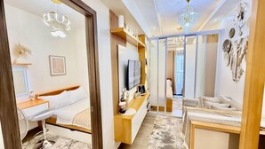 A modern hotel room with a bed, a desk, a TV, and a seating area with a view of the city. - Cozy and Comfy Retreat with Balcony (Paranaque)