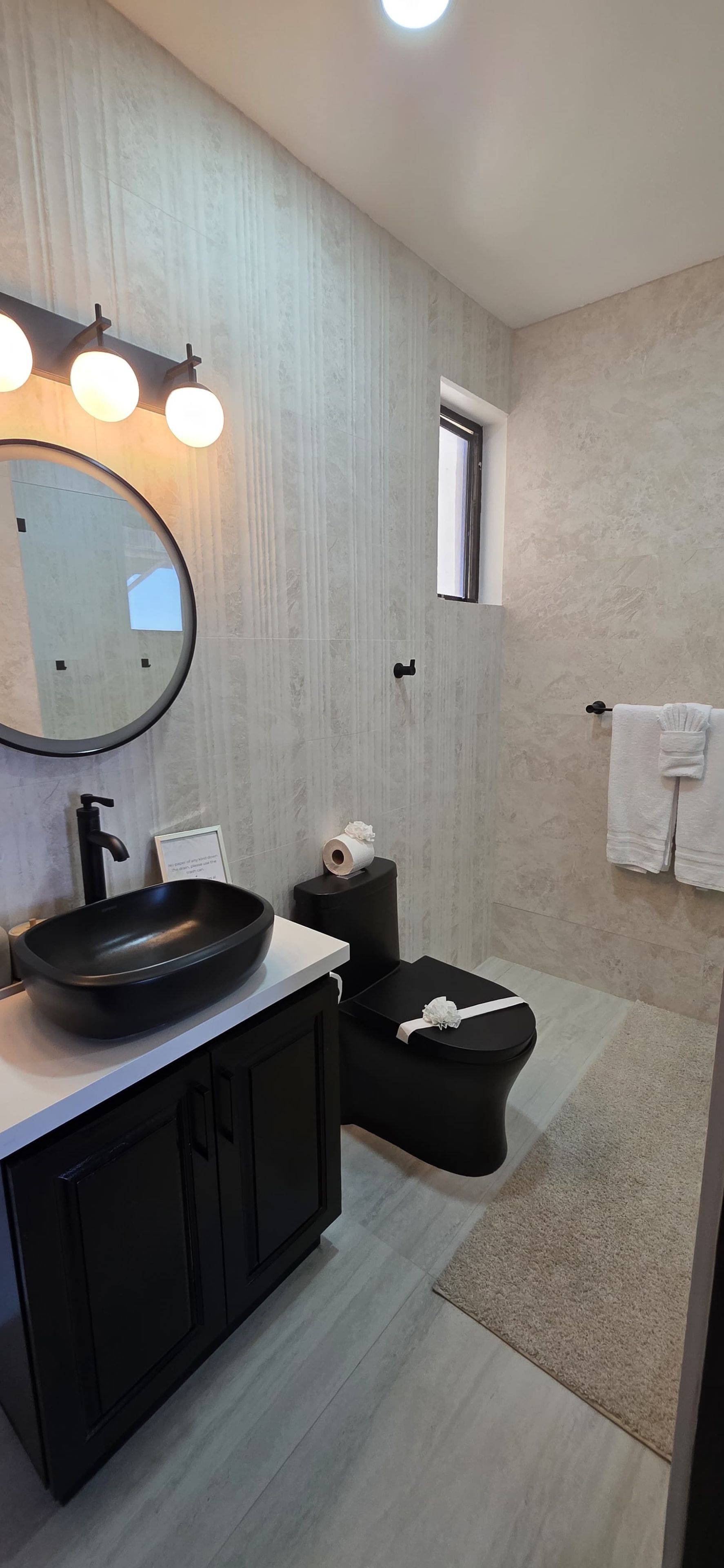 A modern bathroom with a round mirror, black sink, and a toilet.
