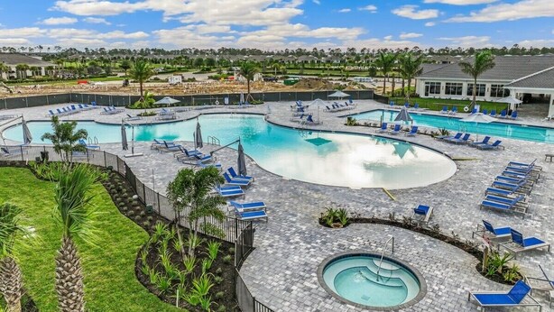 A large outdoor swimming pool with multiple lanes and lounge areas with blue chairs and umbrellas. - Babcock National Golf Club - 2 Bedroom Condo w/ Amenities in Babcock Ranch (Punta Gorda)