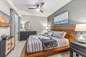 Un dormitorio con cama, mesitas de noche, ventilador de techo, un cuadro y ventana con cortinas.