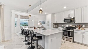 A modern kitchen with white cabinets, a large island with bar stools, stainless steel appliances, and pendant lighting. - Babcock National Golf Club - 2 Bedroom Condo w/ Amenities in Babcock Ranch (Punta Gorda)