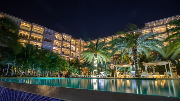 A hotel with a swimming pool, palm trees, and a well-lit building facade. - Ocean views of #1 rated Eagle Beach from 5th floor (Eagle Beach, Oranjestad)