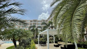 A resort courtyard with a pool, palm trees, outdoor seating, and a building in the background. - Ocean views of #1 rated Eagle Beach from 5th floor (Eagle Beach, Oranjestad)