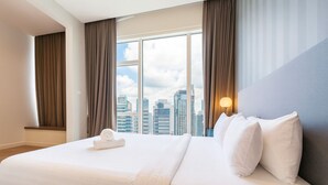 Ein Hotelzimmer mit einem großen Bett, Blick auf die Stadtlandschaft und einem Nachttisch mit Lampe.