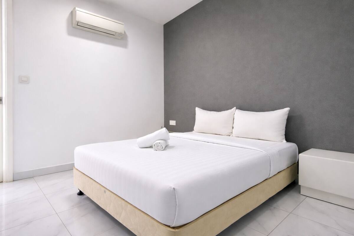 A modern hotel room with a large bed, white bedding, and a grey accent wall.