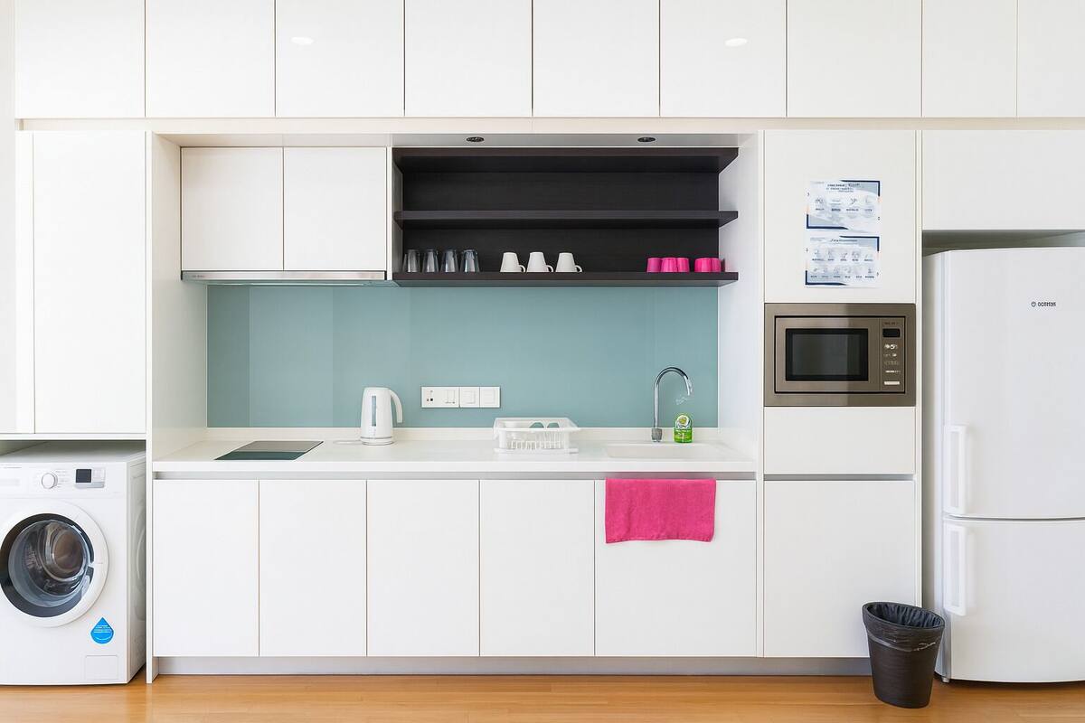 A modern kitchen with white cabinets, a built-in washing machine, a microwave, and a refrigerator.