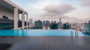 Ein Infinity-Pool auf dem Dach mit Blick auf die Stadtlandschaft, einer Holzterrasse und moderner Architektur.