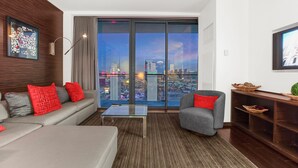 Un salon moderne avec un canapé, des fauteuils, une table basse et une vue sur le paysage urbain grâce à de grandes fenêtres.