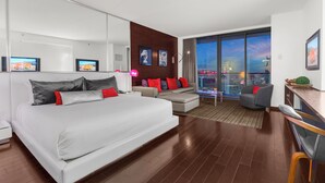 Une chambre d’hôtel moderne dotée d’un grand lit, d’un canapé, d’un bureau et offrant une vue sur la ville à travers la porte vitrée.