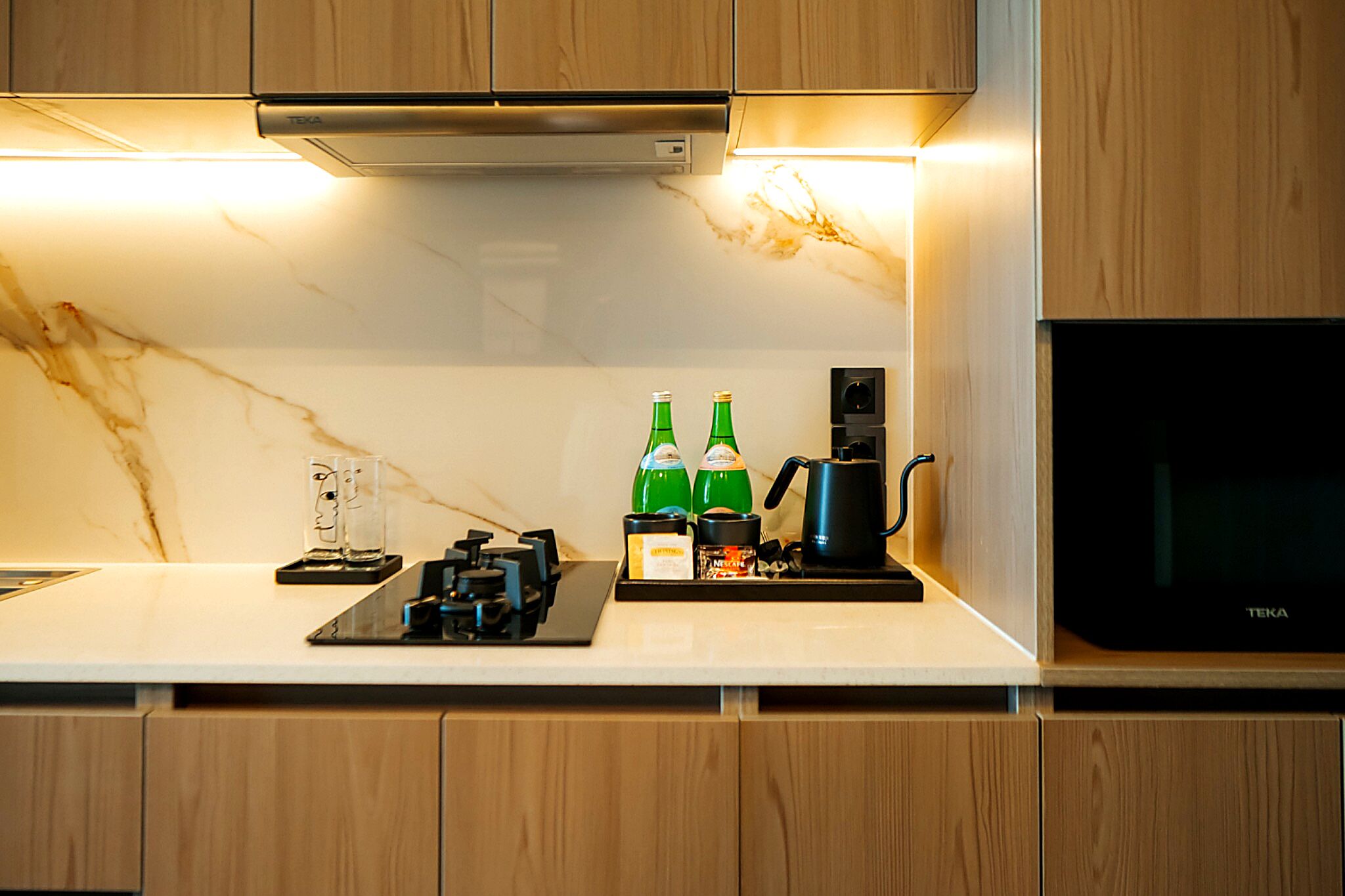 A modern kitchen with a marble countertop, wooden cabinets, a black coffee maker, and two green bottles.