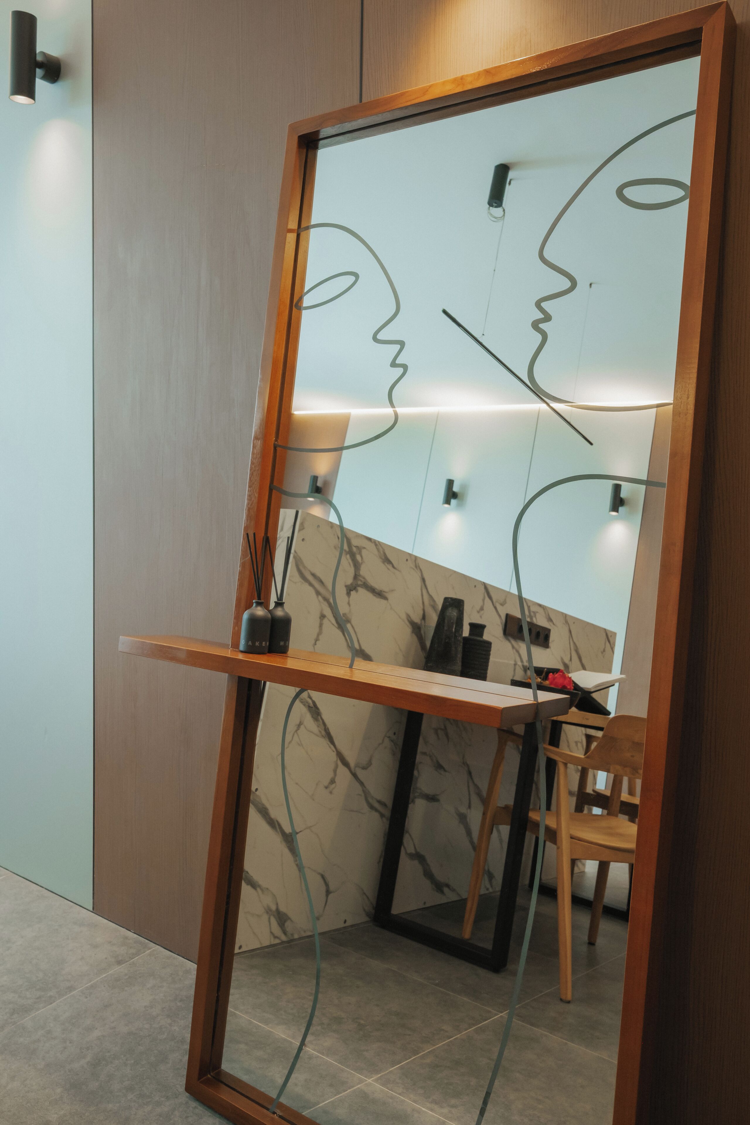 A room with a wooden-framed mirror, a marble-patterned wall, a small table, and a chair.