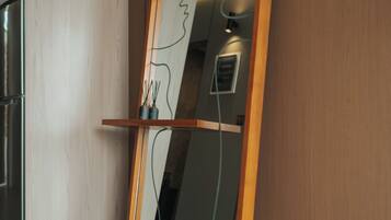 Een spiegel met houten lijst, geleund tegen een muur, met een lamp erboven.
