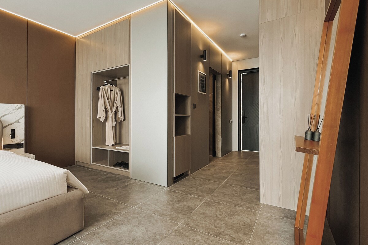 A modern hotel room with a bed, built-in wardrobe, and a wooden sideboard.