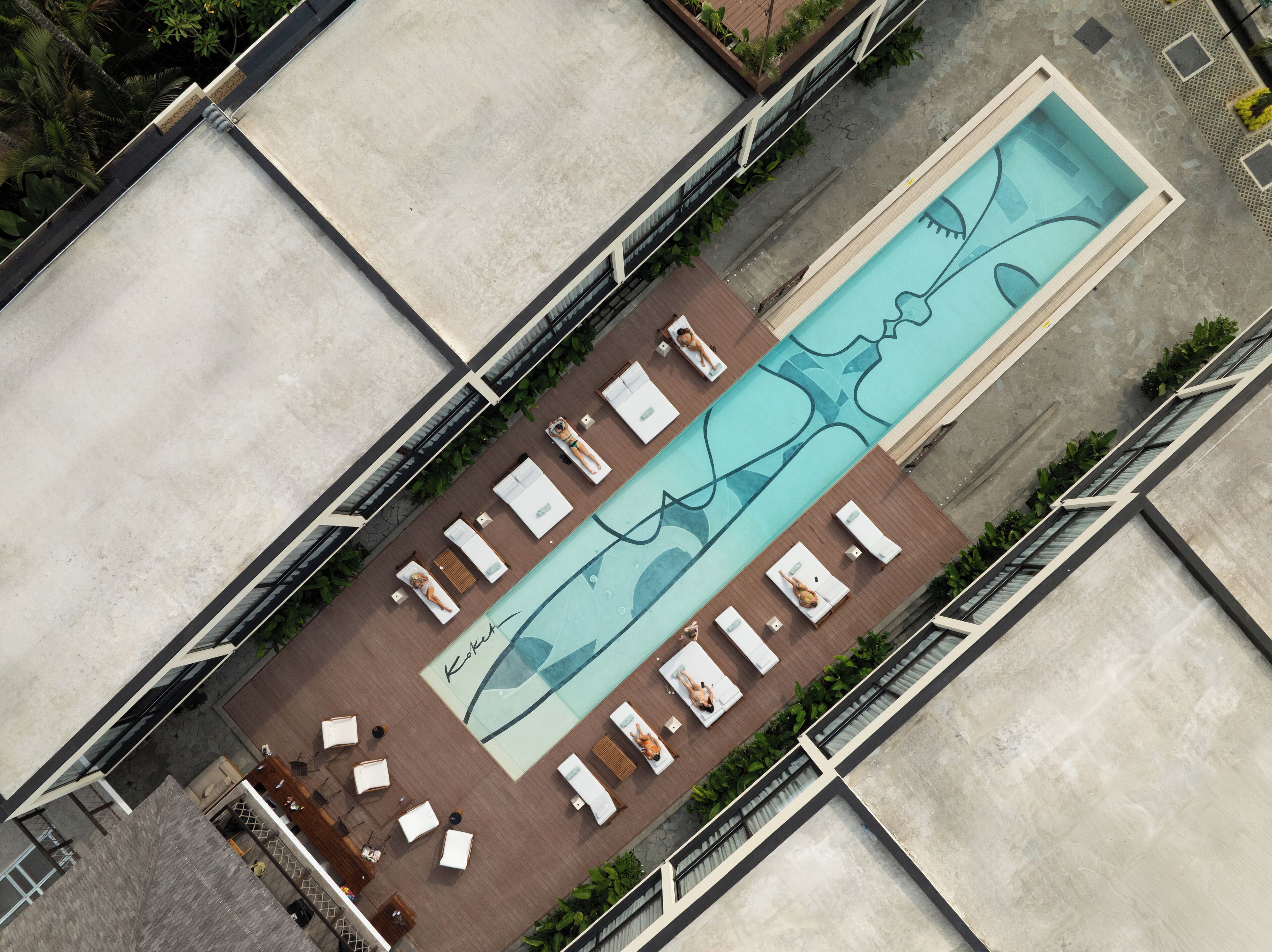 An aerial view of a hotel with a long swimming pool, multiple sun loungers, and a covered seating area.