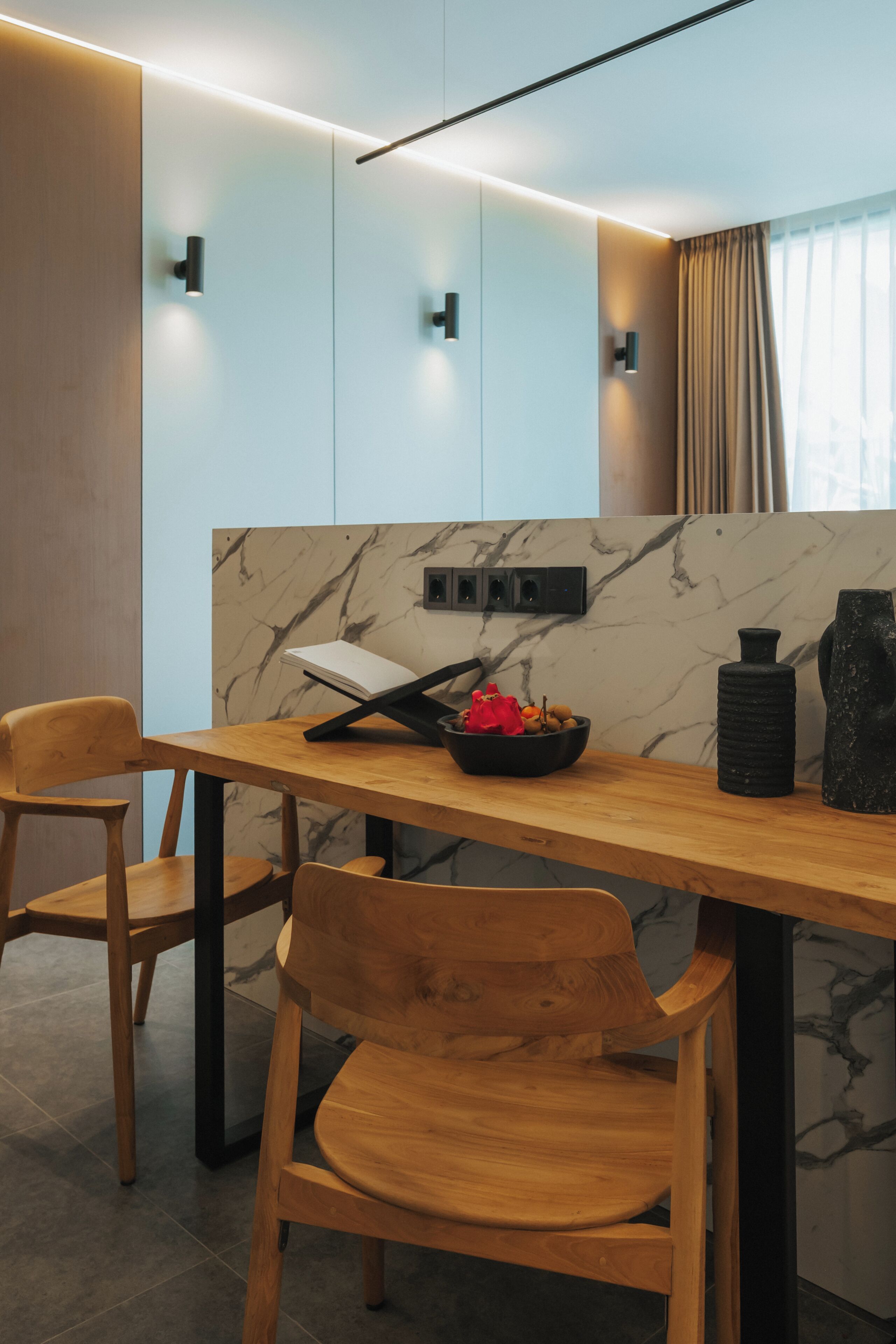 Un comedor moderno con una mesa y sillas de madera, un salpicadero de mármol y un jarrón negro.