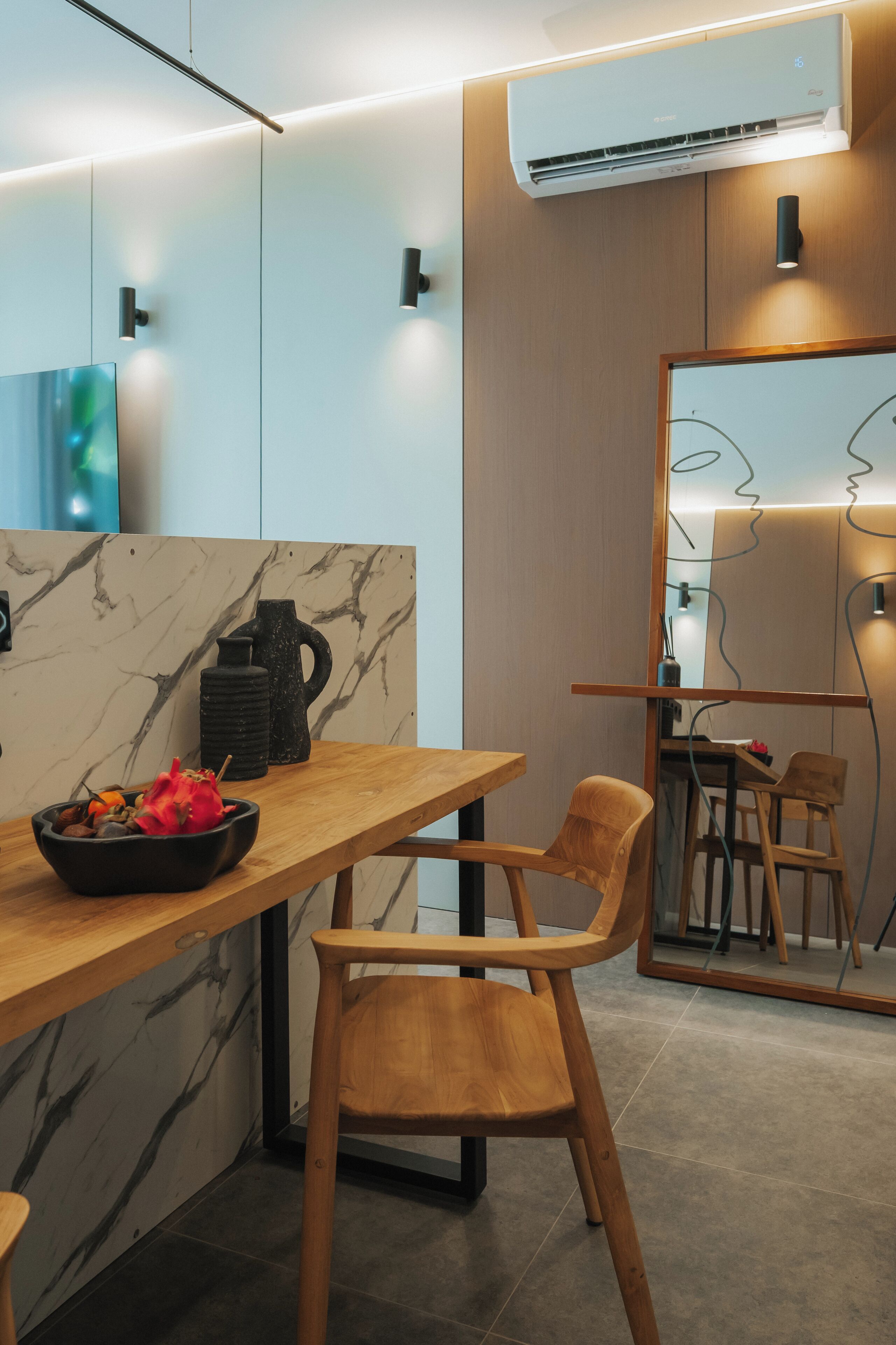 Une cuisine moderne avec un plan de travail en marbre, des chaises en bois et un saladier noir rempli de fruits.