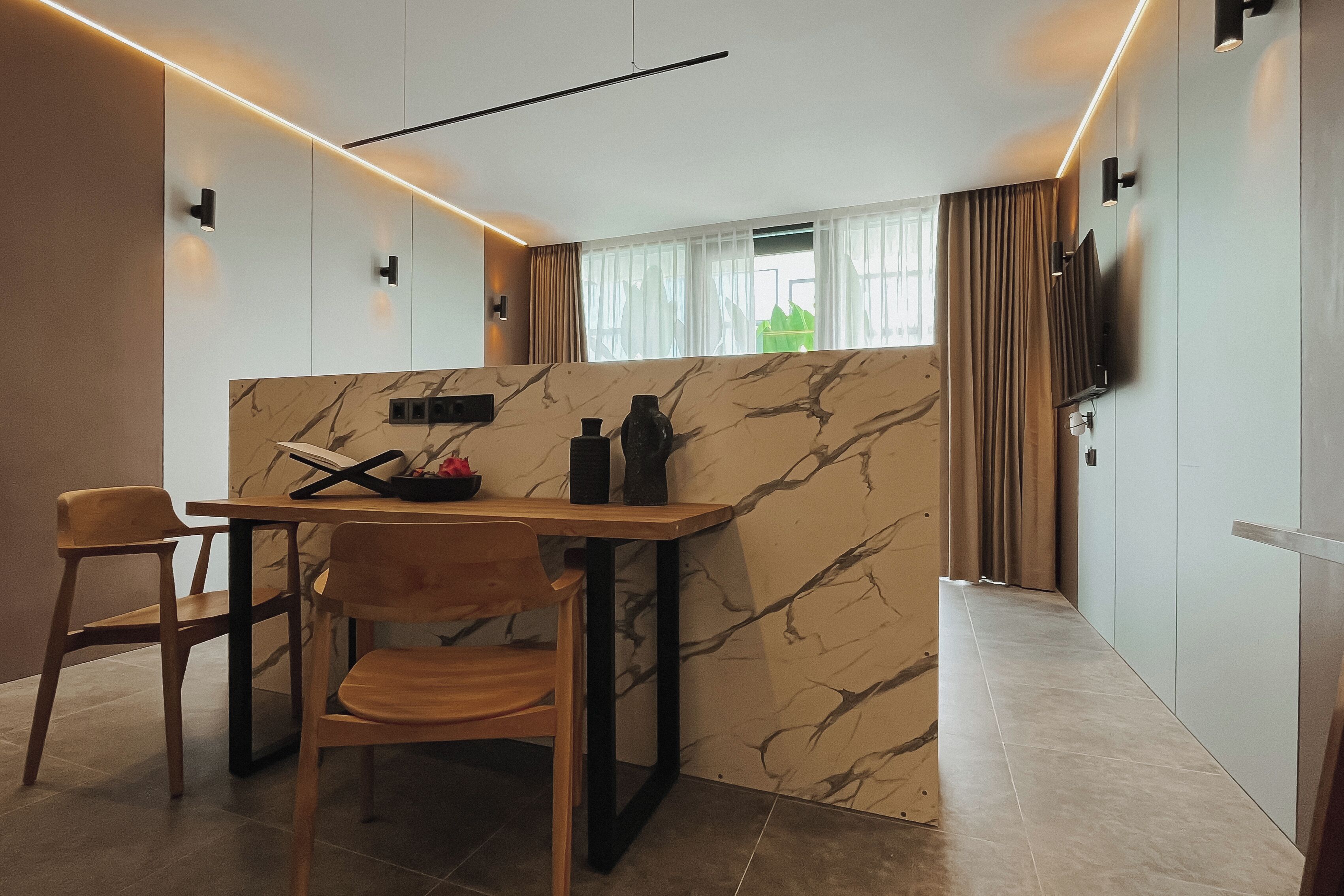 Een moderne keuken met een marmeren achterwand, houten stoelen, een eettafel en een aan de muur bevestigde televisie.