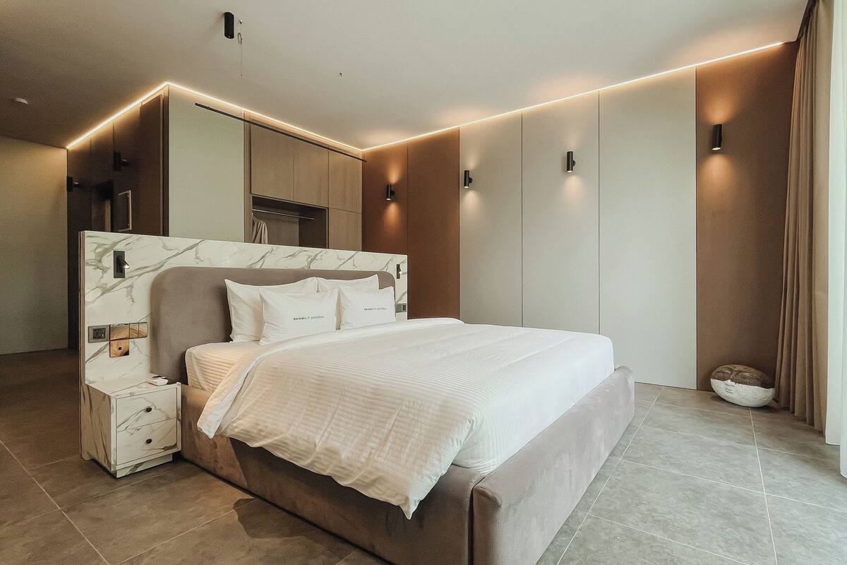 A modern bedroom with a marble headboard, a large bed, bedside tables, and built-in lighting.