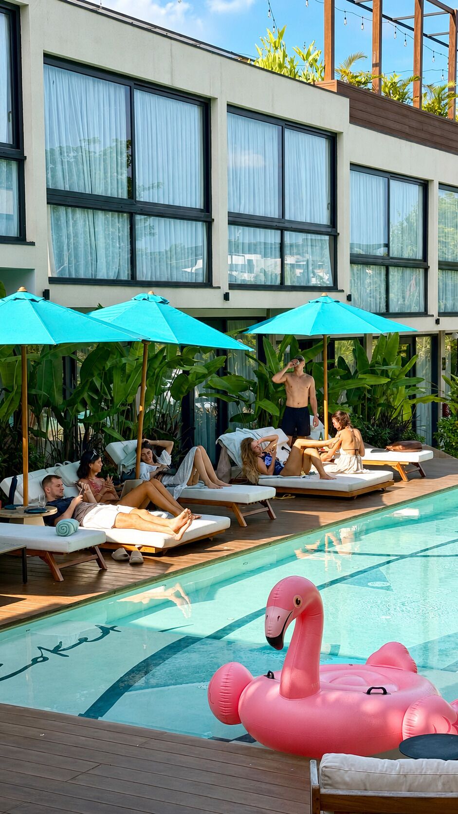 A pool area with lounge chairs, umbrellas, and a pink flamingo float.