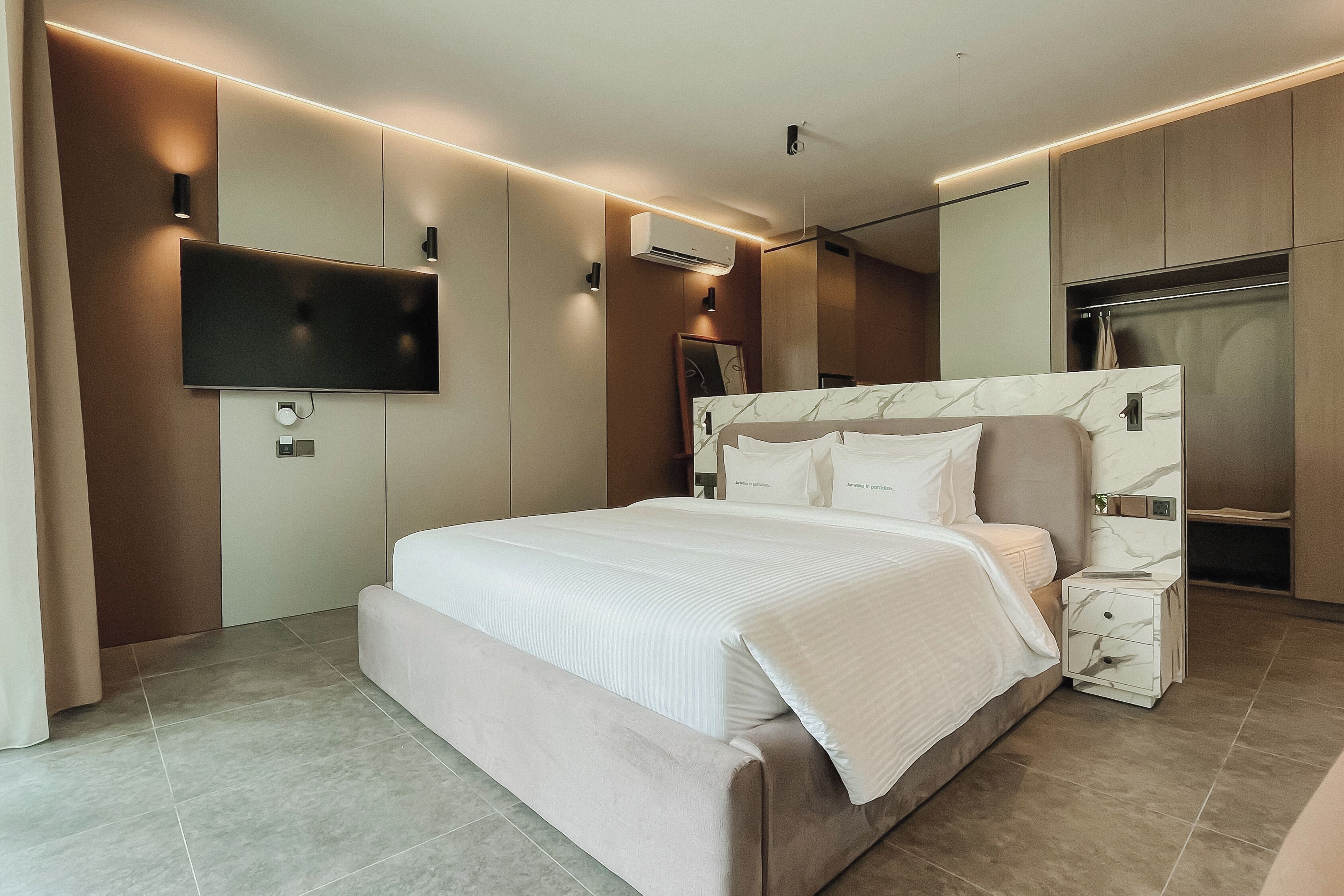 A modern bedroom with a large bed, a flat-screen TV mounted on the wall, and a built-in wardrobe.