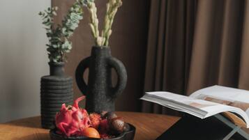 A round wooden table with a black vase containing dried flowers, a bowl with fruits, and a book.