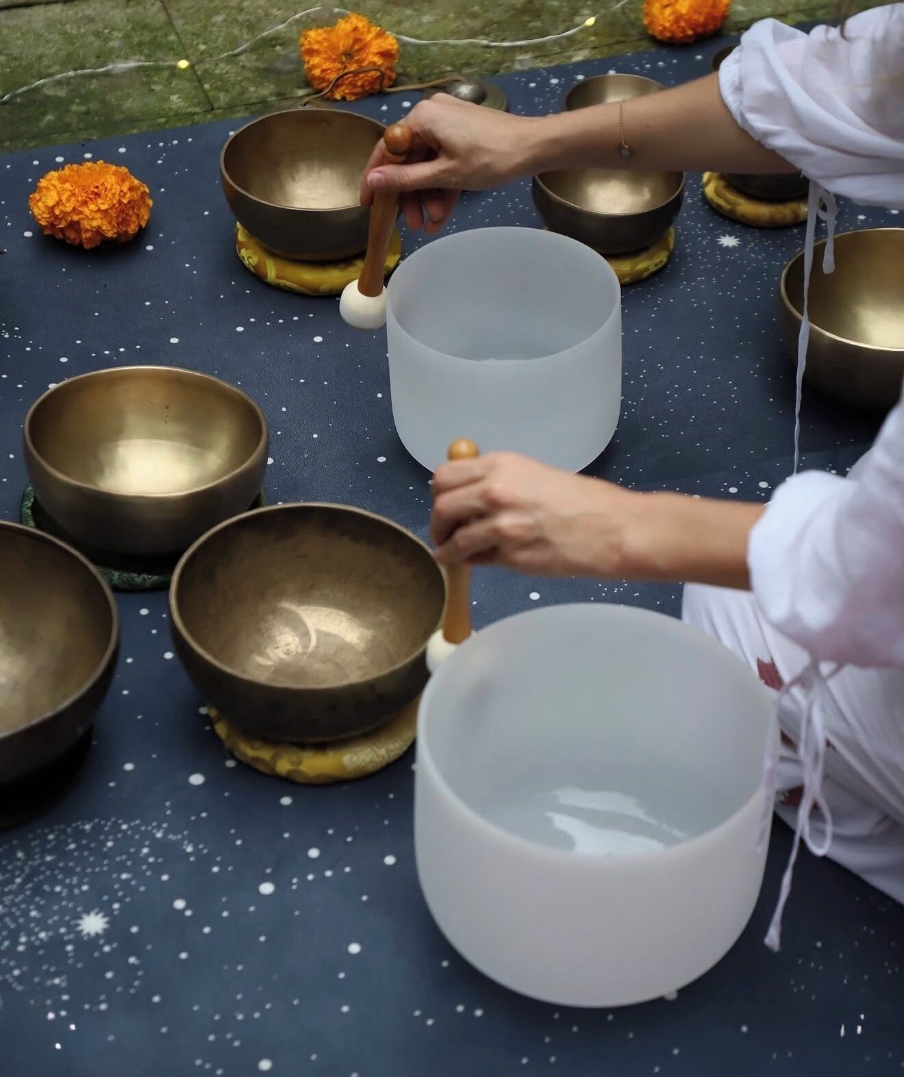 Una persona suona un grande tamburo all'aperto, circondata da diversi tamburi più piccoli e fiori di calendula.