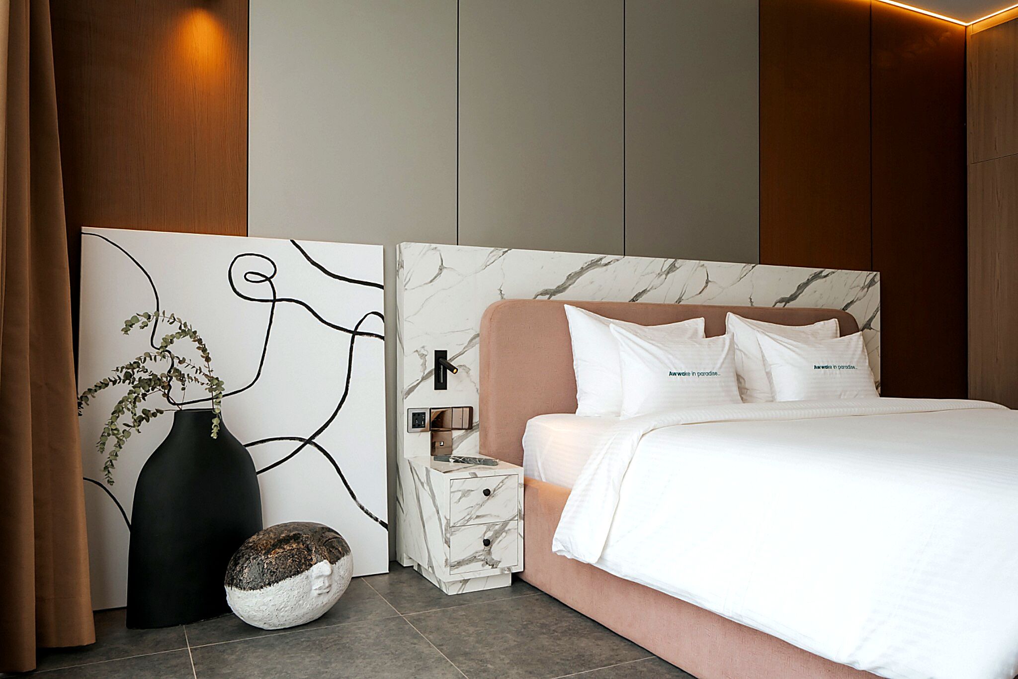 A modern bedroom with a marble headboard, a bedside table with a vase and a decorative rock, and a wall art piece.