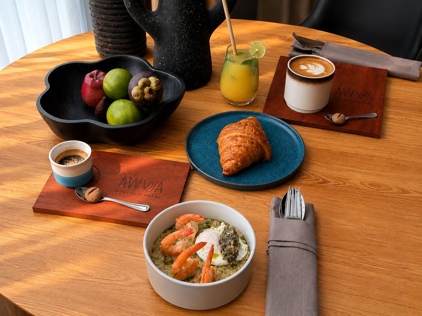 A wooden table with a bowl of shrimp, a croissant, a coffee cup, a fruit bowl, a glass of juice, and a sign for 'AWVIA Boutique Hotel'.