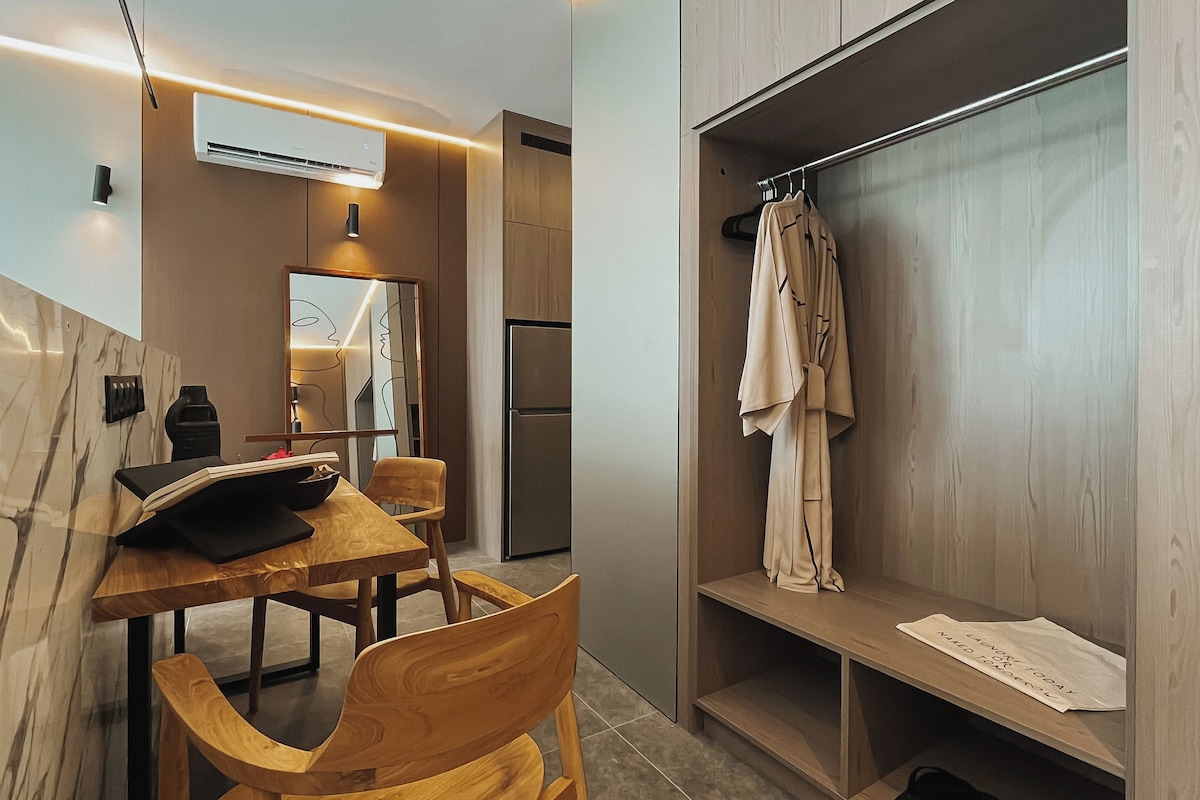 Una cocina moderna con una mesa de comedor y sillas, un refrigerador y un armario de madera con ropa colgada.