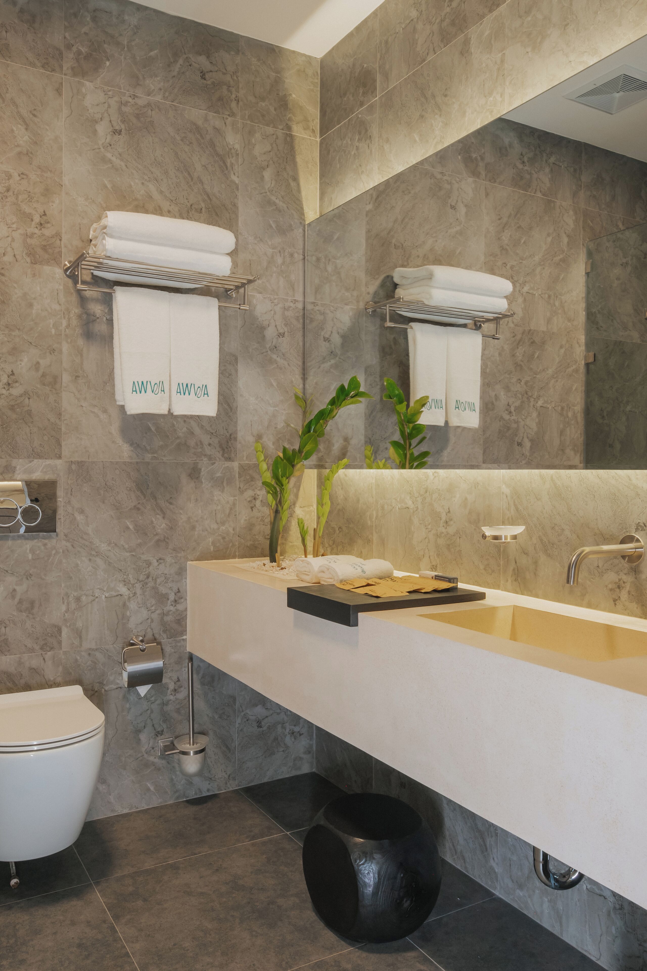 A modern bathroom with a marble wall, a white sink, a mirror, and a toilet.