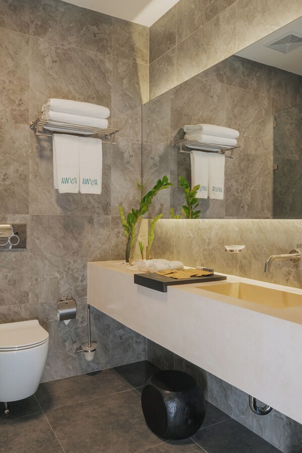 Un baño moderno con pared de mármol, un lavamanos blanco, un espejo y un inodoro.