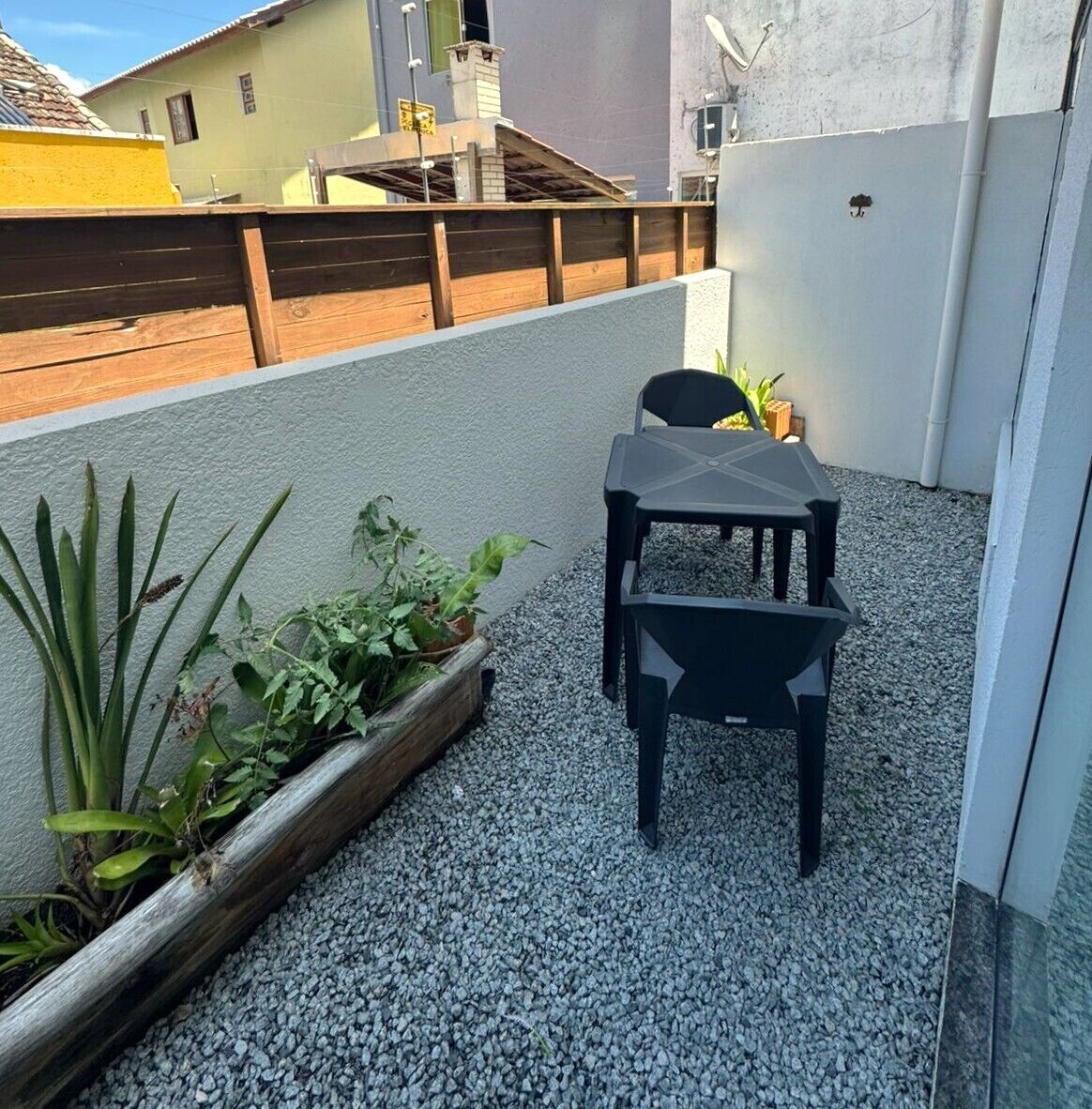 Een klein terras buiten met een tafel en stoelen, omringd door grind en potplanten.